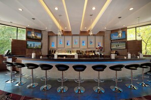 A modern bar area with a long counter, multiple bar stools, and a selection of bottles. - Holiday Inn Express Princeton Southeast by IHG (Plainsboro)