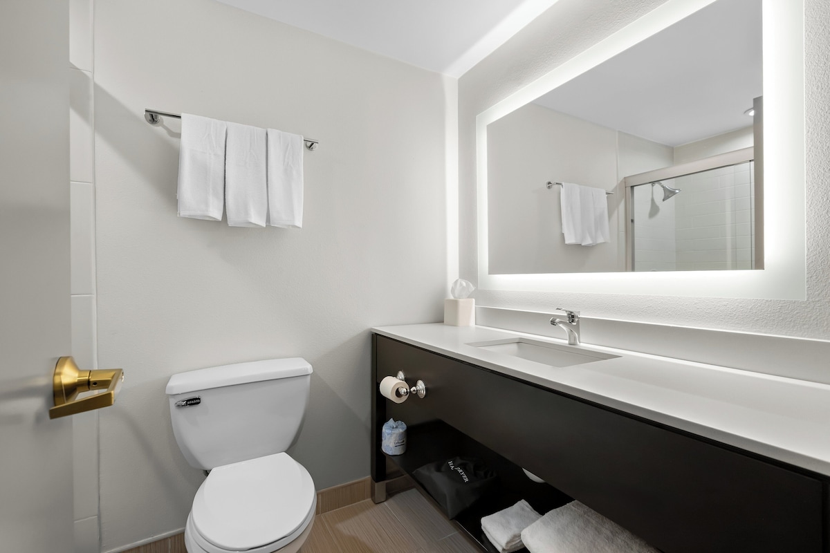 Une salle de bain moderne avec des toilettes blanches, un lavabo surmonté d’un miroir et un porte-serviettes.