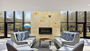 A modern outdoor seating area with two sofas and a coffee table, a stone fireplace, and large windows offering a view of trees and a building. - Holiday Inn Express Princeton Southeast by IHG (Plainsboro)