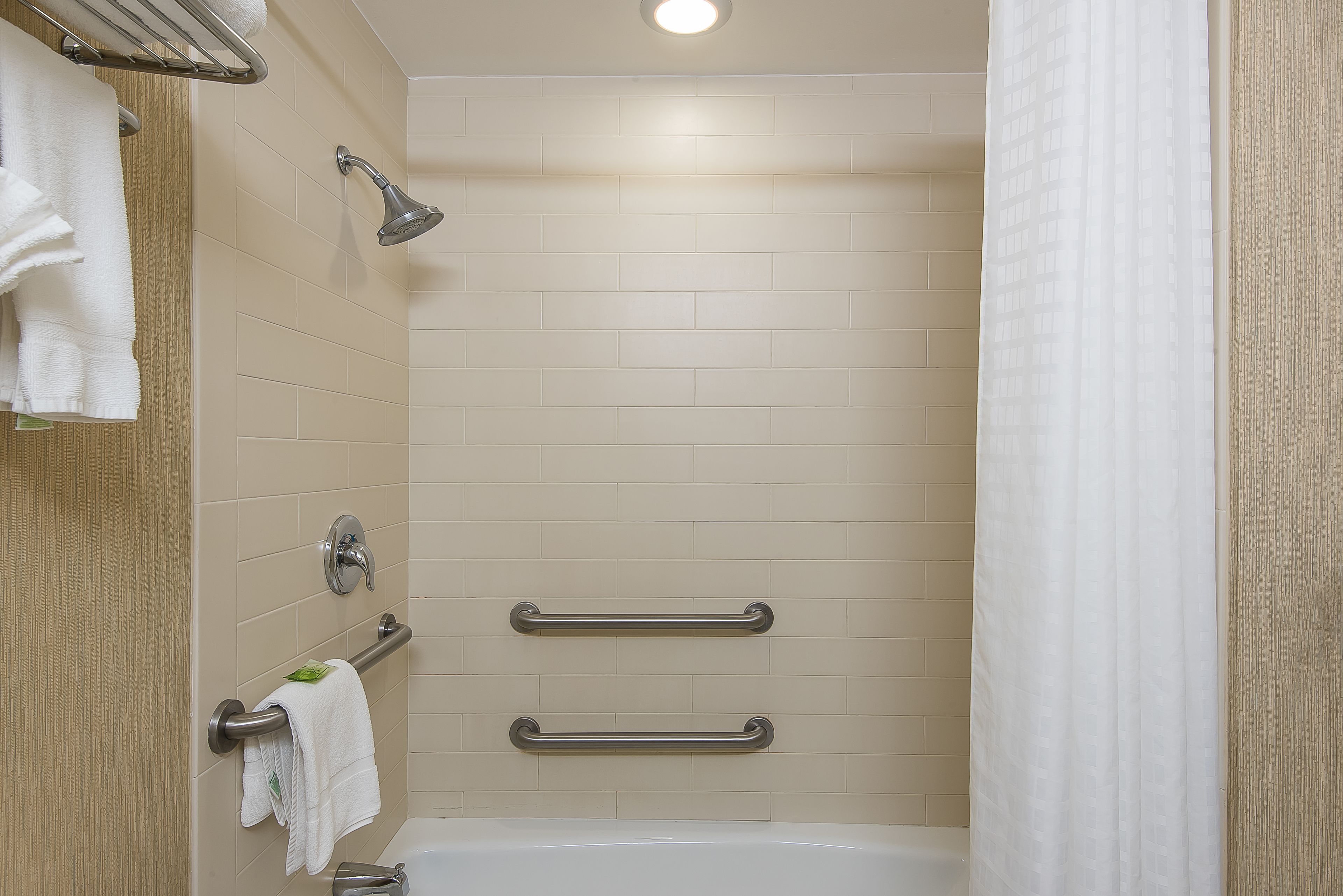 A shower area with a handheld showerhead, grab bars, and a white bathtub.