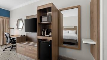 Hotelkamer met een houten bureau, een zwarte koelkast, een flatscreen televisie, een bed met witte lakens en een grote spiegel.