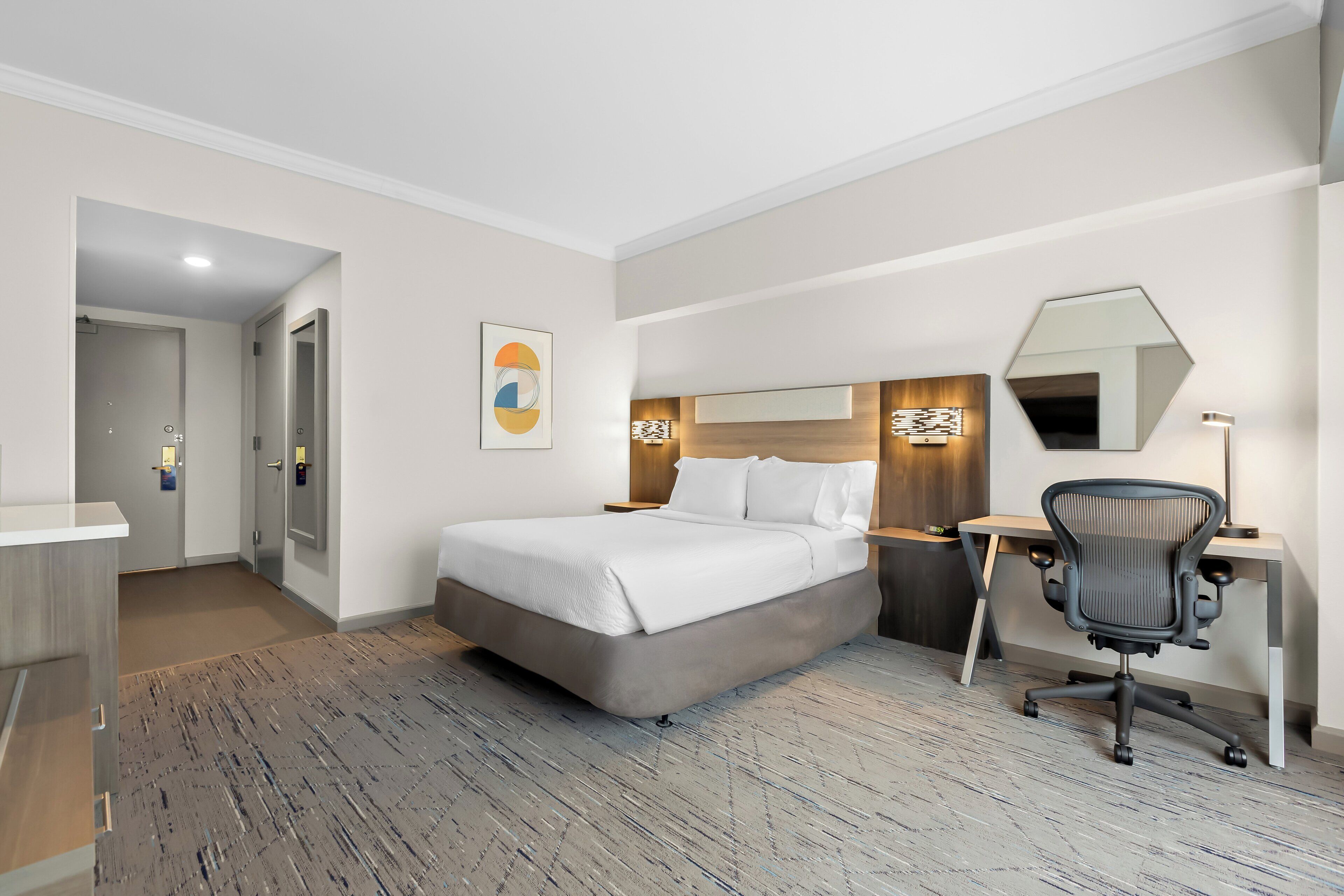 A modern hotel room with a large bed, a desk, and a chair.