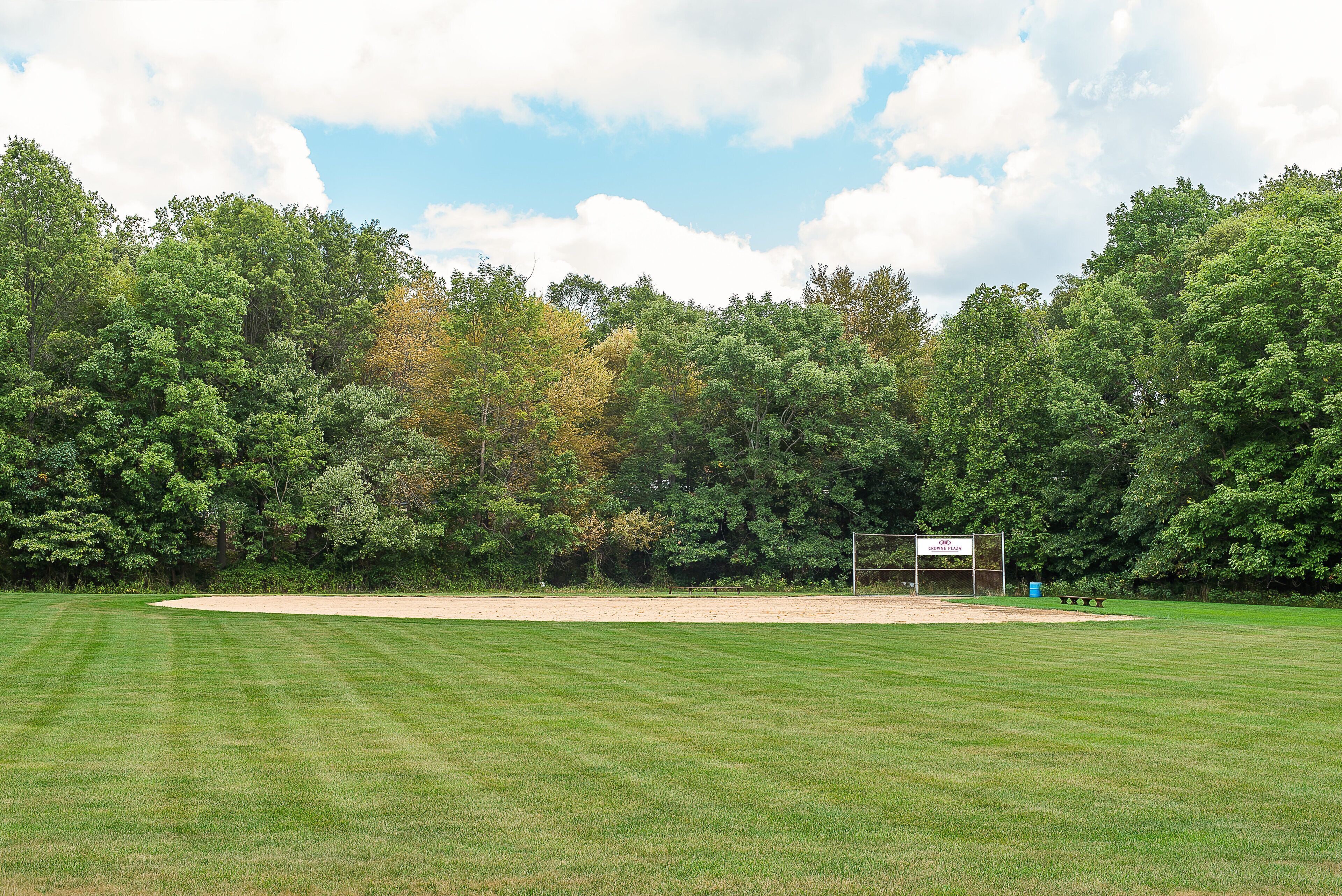 A golf course with a sand bunker, a sign reading 'CROWNE PLAZA,' and a dense backdrop of trees.