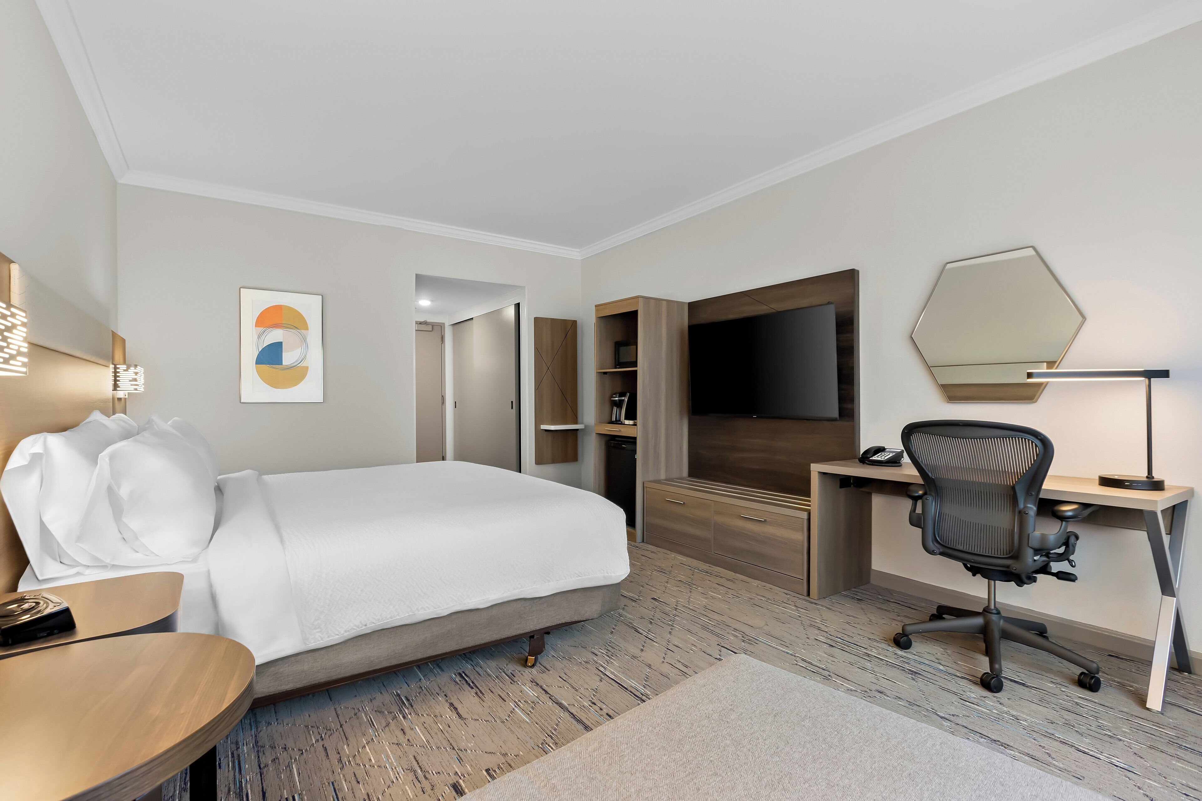 Une chambre d’hôtel avec un lit, un bureau, une chaise et un grand miroir.