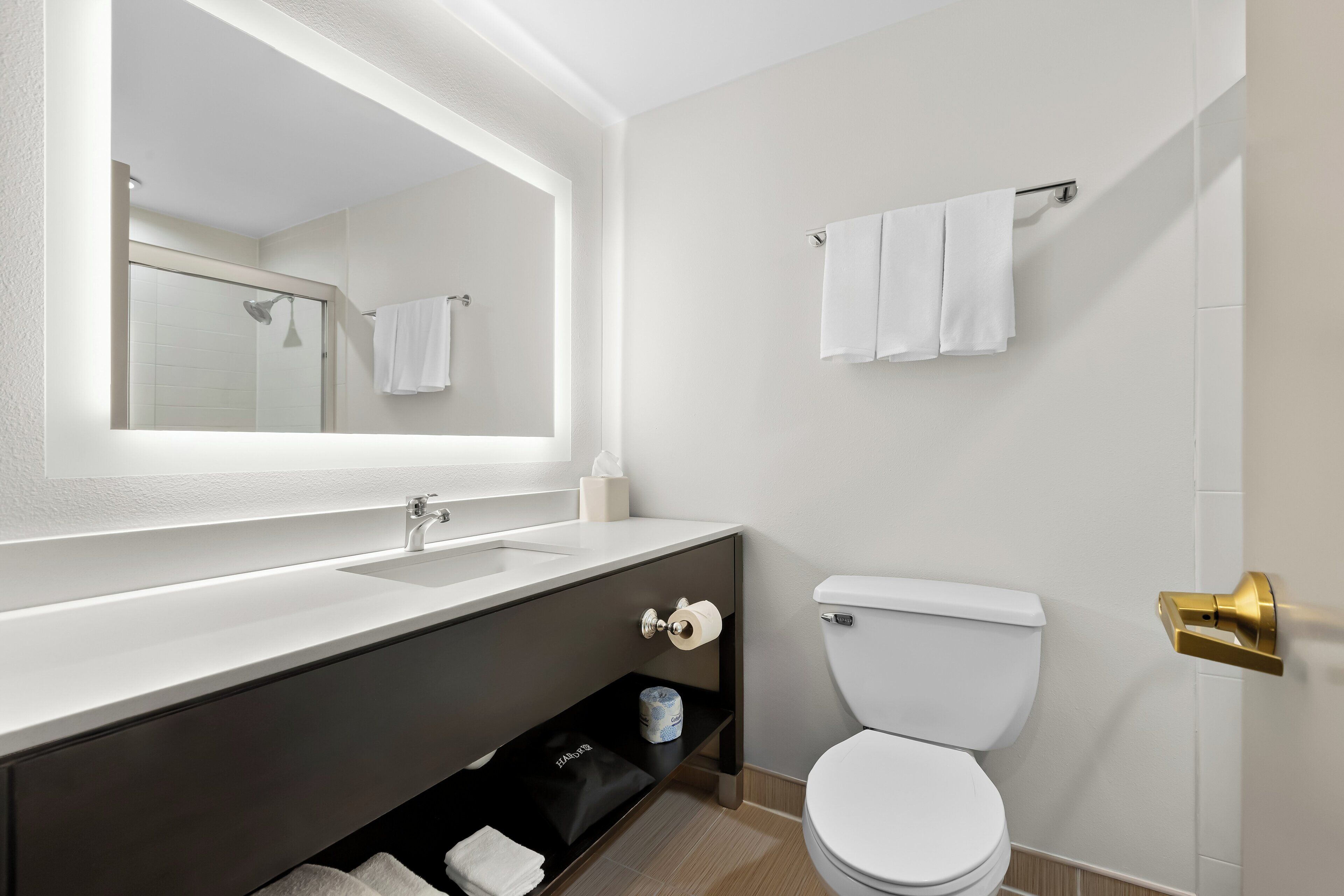 A modern bathroom with a white sink, a large mirror, a toilet, and a towel rack.