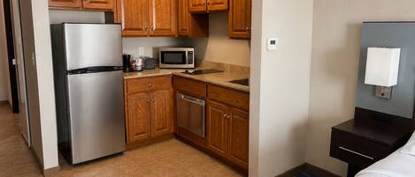 A compact hotel room with a kitchenette, including a refrigerator, microwave, and dishwasher.
