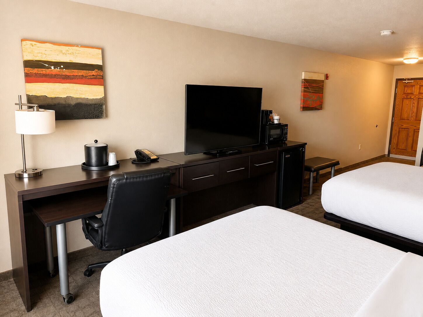 A hotel room with a desk, a television, a bed, and a small kitchenette.