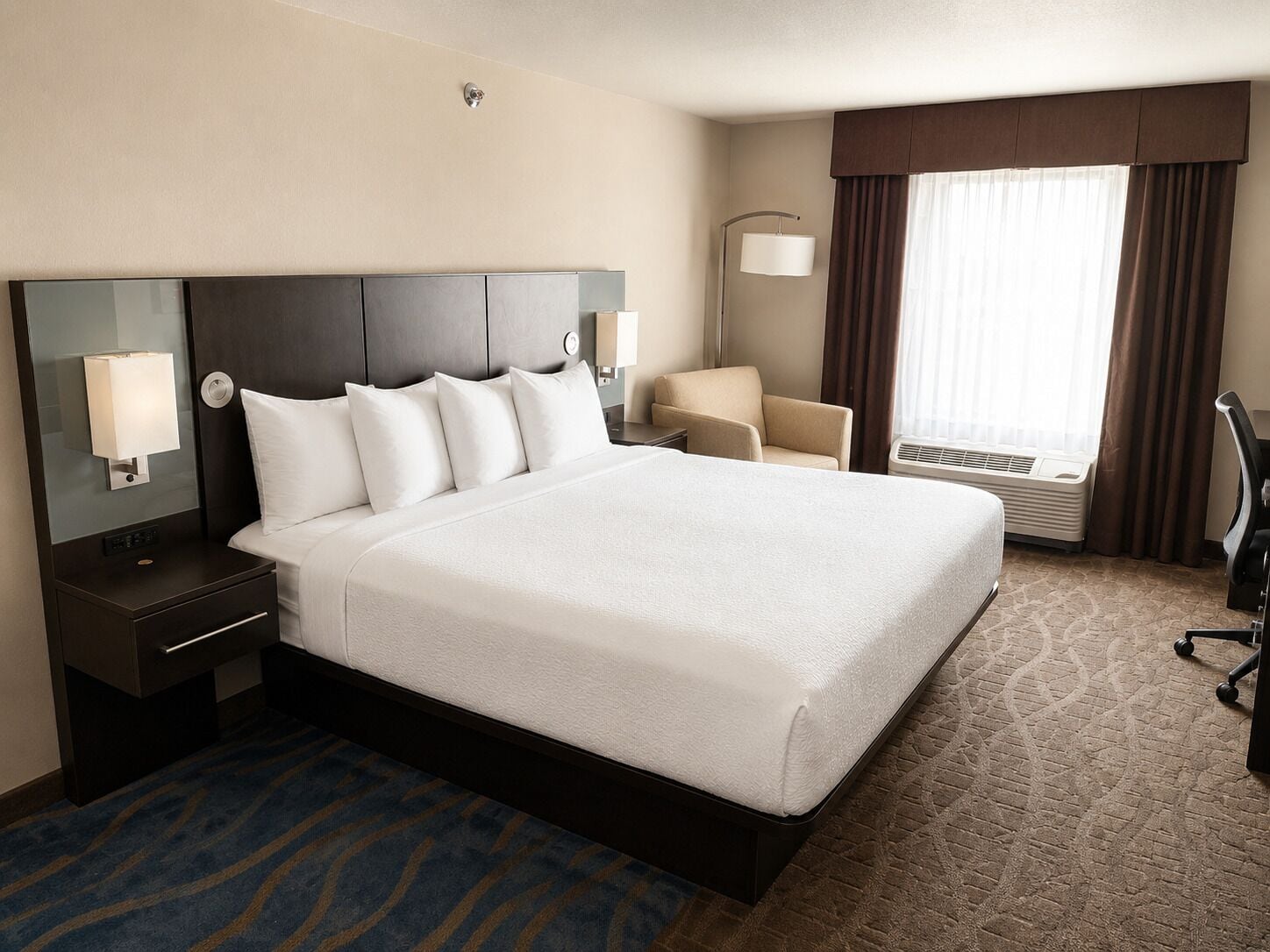 A hotel room with a large bed, a desk, a chair, and a window with curtains.