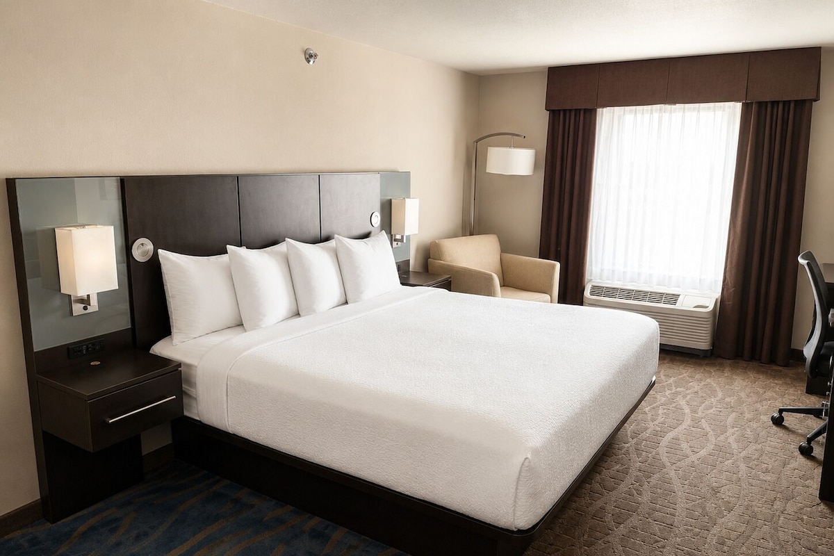 A hotel room with a large bed, a desk, a chair, and a window with curtains.