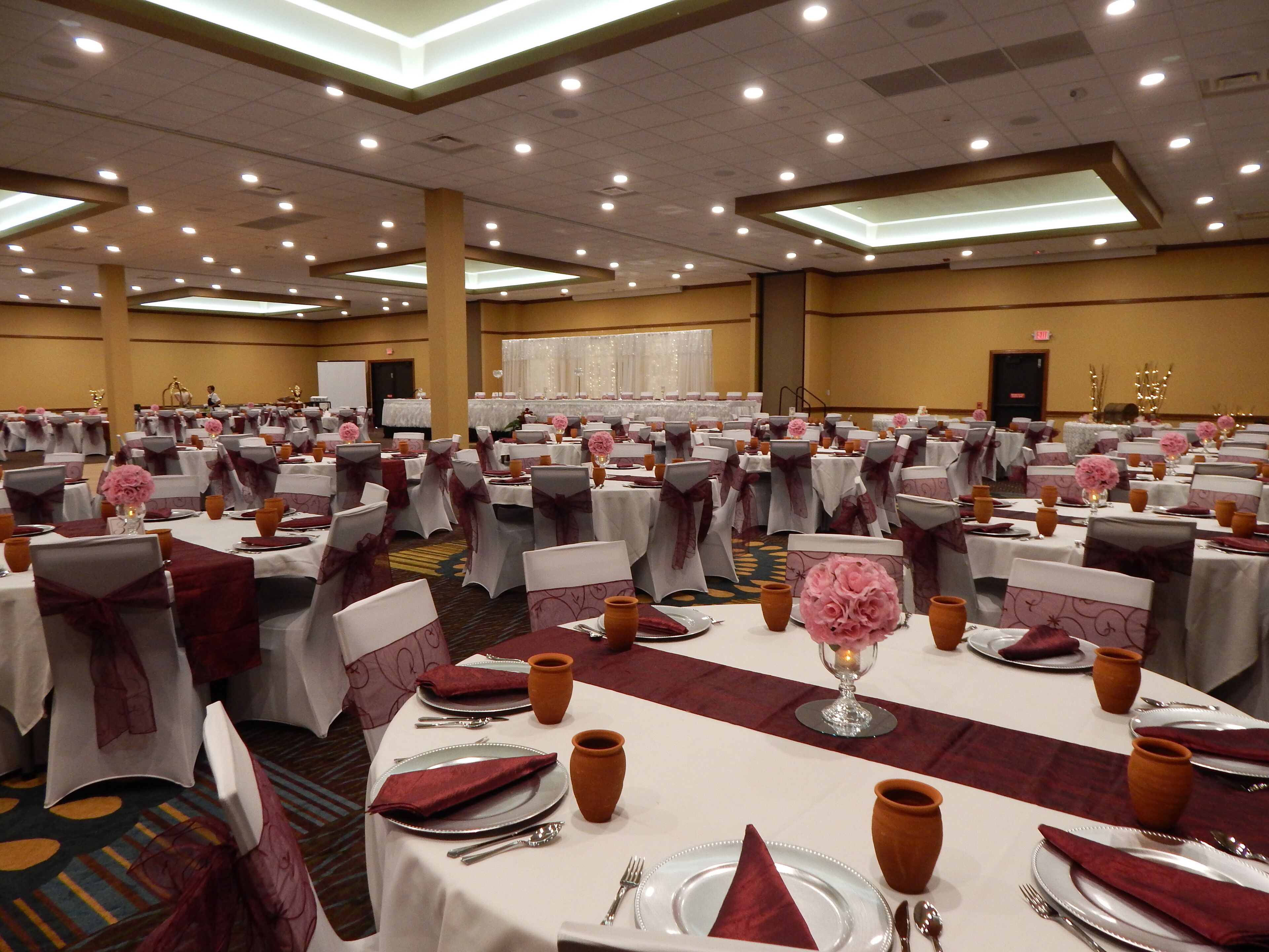 Un salón de banquetes con mesas redondas, cada una dispuesta con platos, cubiertos y jarrones.