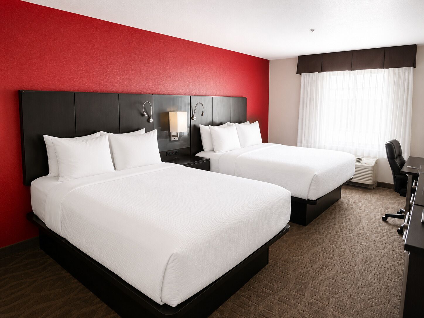 Ein Hotelzimmer mit zwei Betten, einem Schreibtisch, einem Stuhl und einem fenster mit Vorhängen.