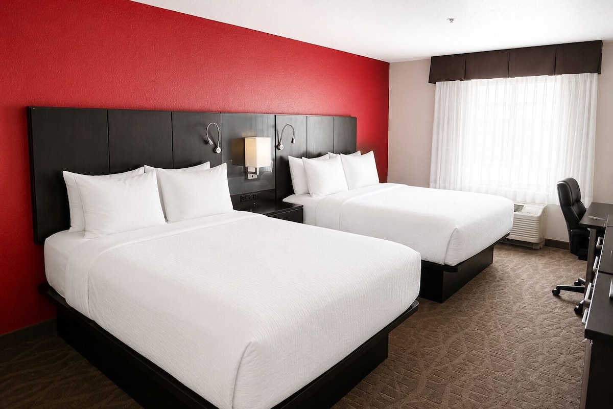 A hotel room with two beds, a desk, a chair, and a window with curtains.