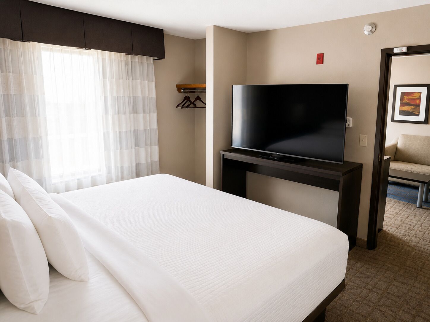 A hotel room with a bed, a television on a stand, a coat rack, and a door leading to another room.
