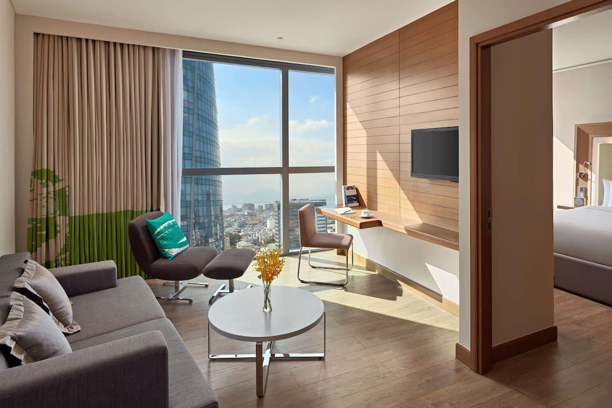 Una habitación de hotel moderna con un ventanal grande, un sofá, un escritorio y una cama.