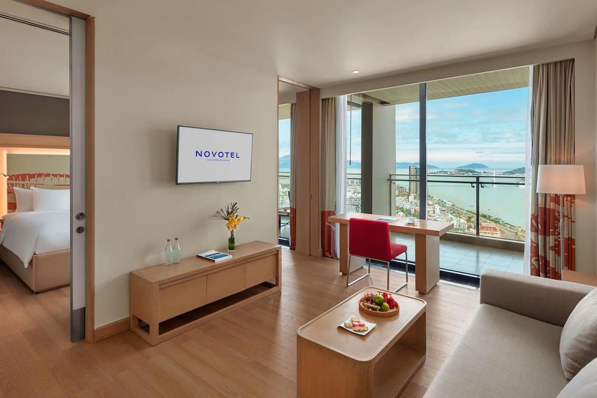 Habitación de hotel con cama, escritorio, silla, sofá, televisor y vistas a la ciudad.