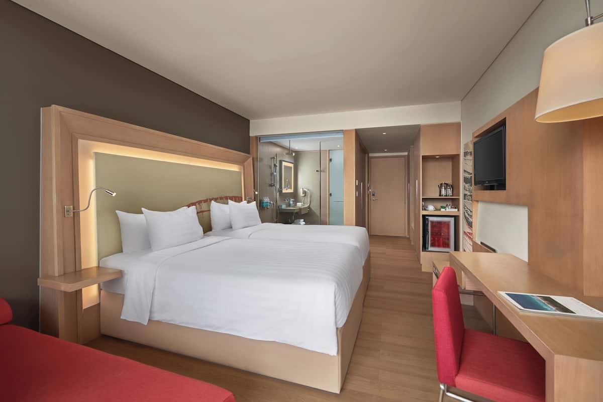 Habitación de hotel con una cama grande, un escritorio, un televisor y una silla roja.