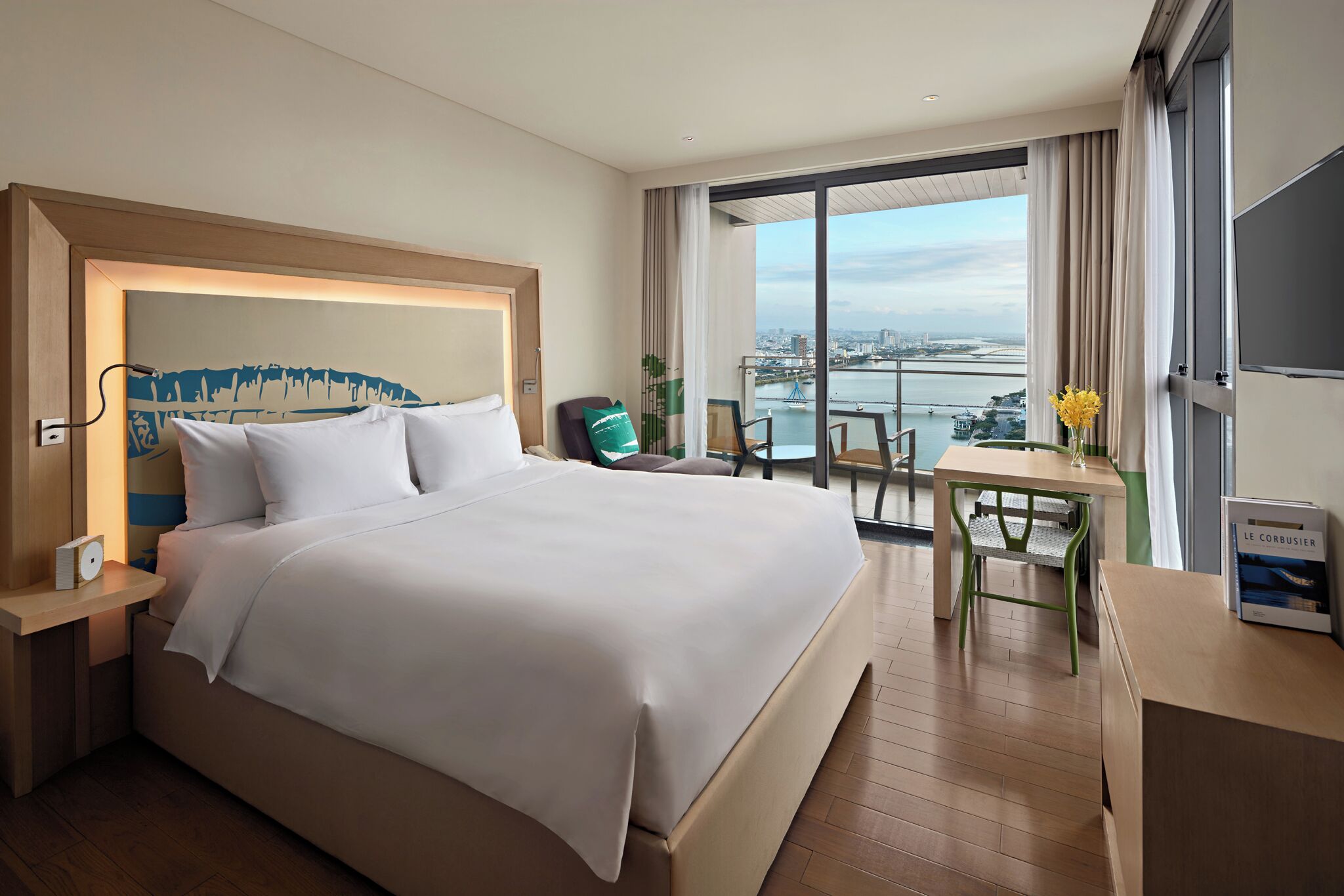 A hotel room with a large bed, a desk, and a view of a cityscape.