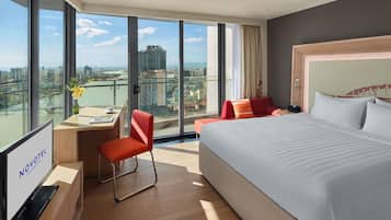 Una habitación de hotel moderna con una cama grande, un escritorio con una silla y vistas a la ciudad a través de amplias ventanas.
