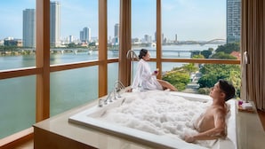 A modern hotel room with a large bathtub, a city view, and a window with curtains. - Novotel Danang Premier Han River (Da Nang)