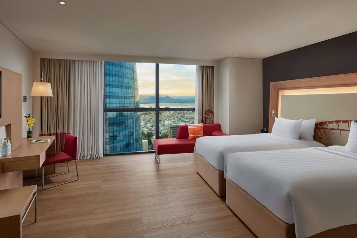 Habitación de hotel con un ventanal grande, un escritorio, dos camas y una silla roja.