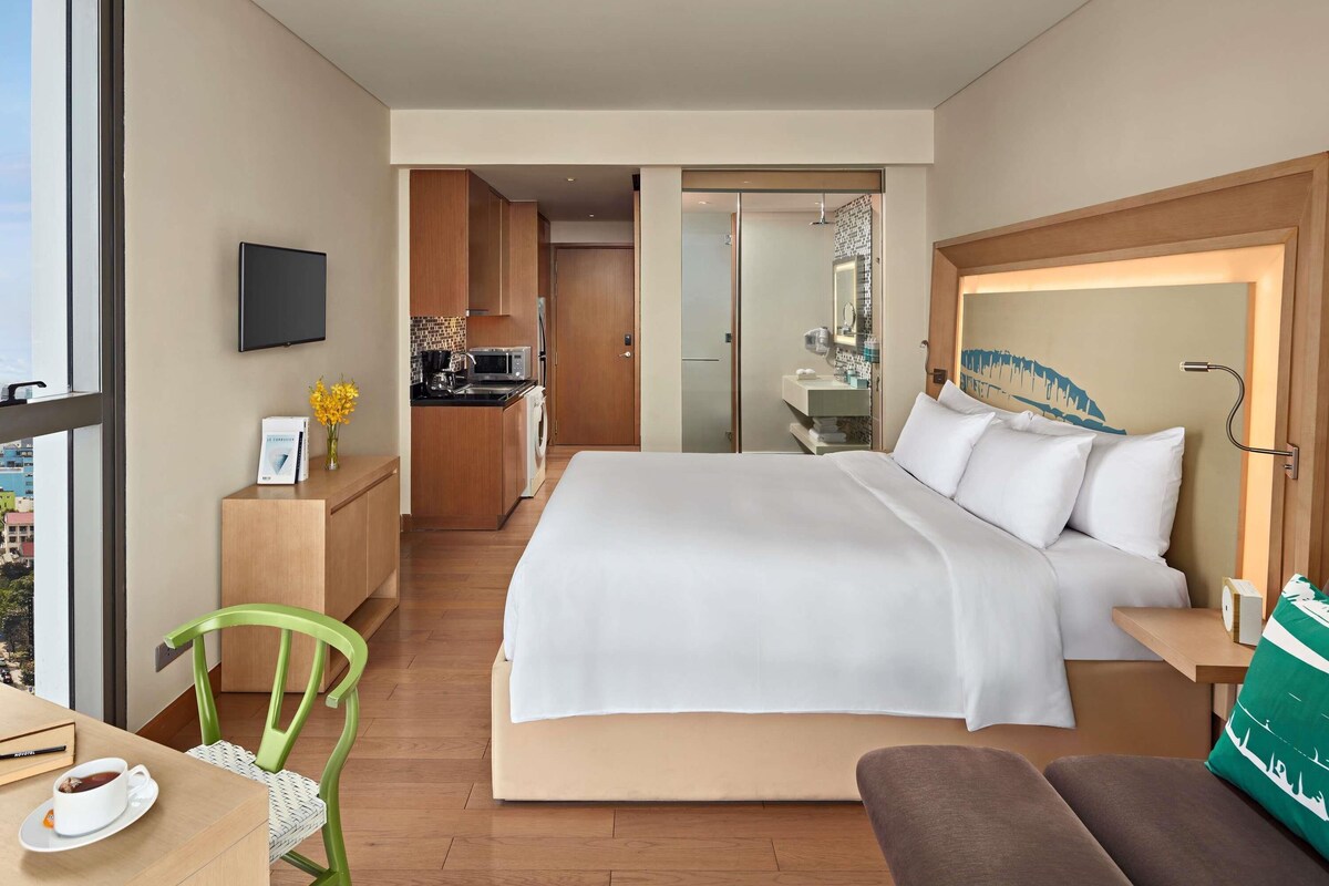 A hotel room with a bed, a desk with a chair, a small kitchenette, and a bathroom.