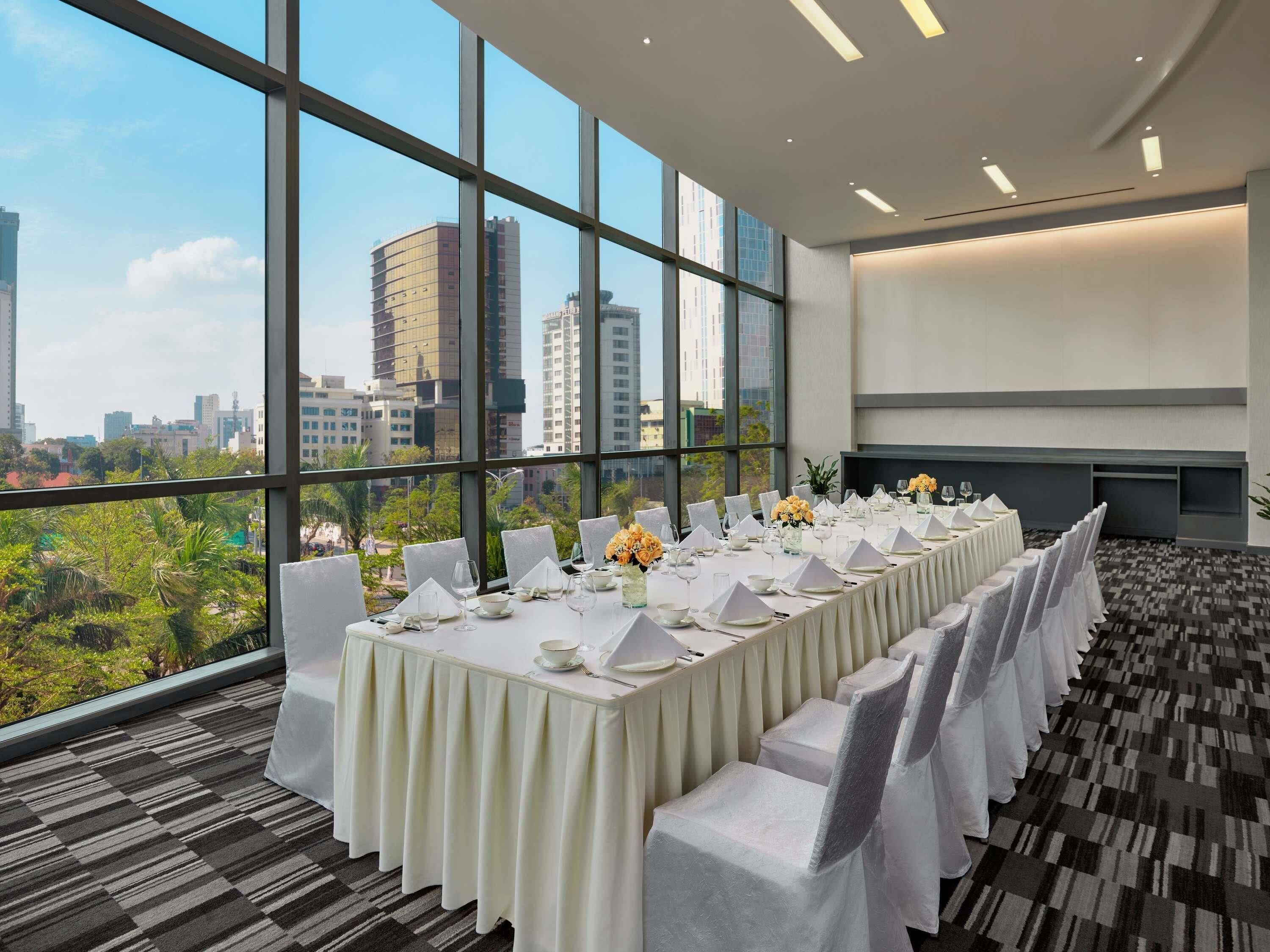 A conference room with a long table set for a meeting, large windows with a city view, and a carpeted floor.