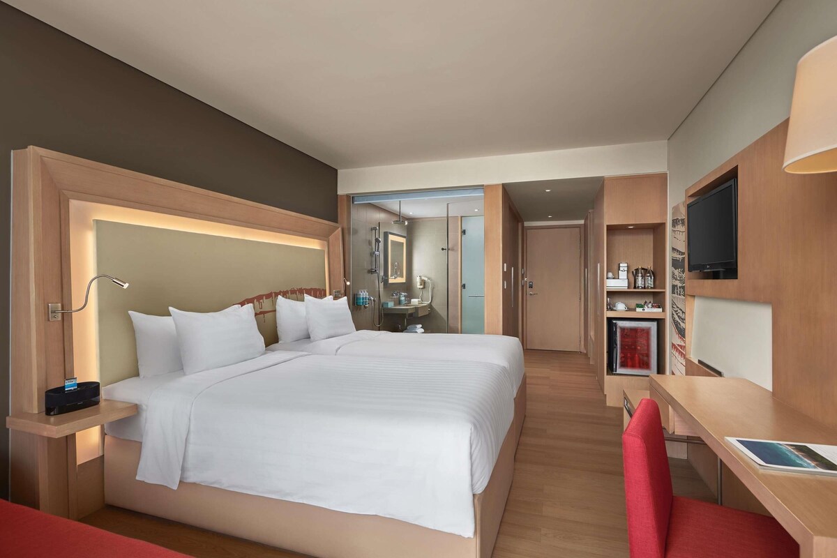 A hotel room with a large bed, a desk, a TV, and a shower area.