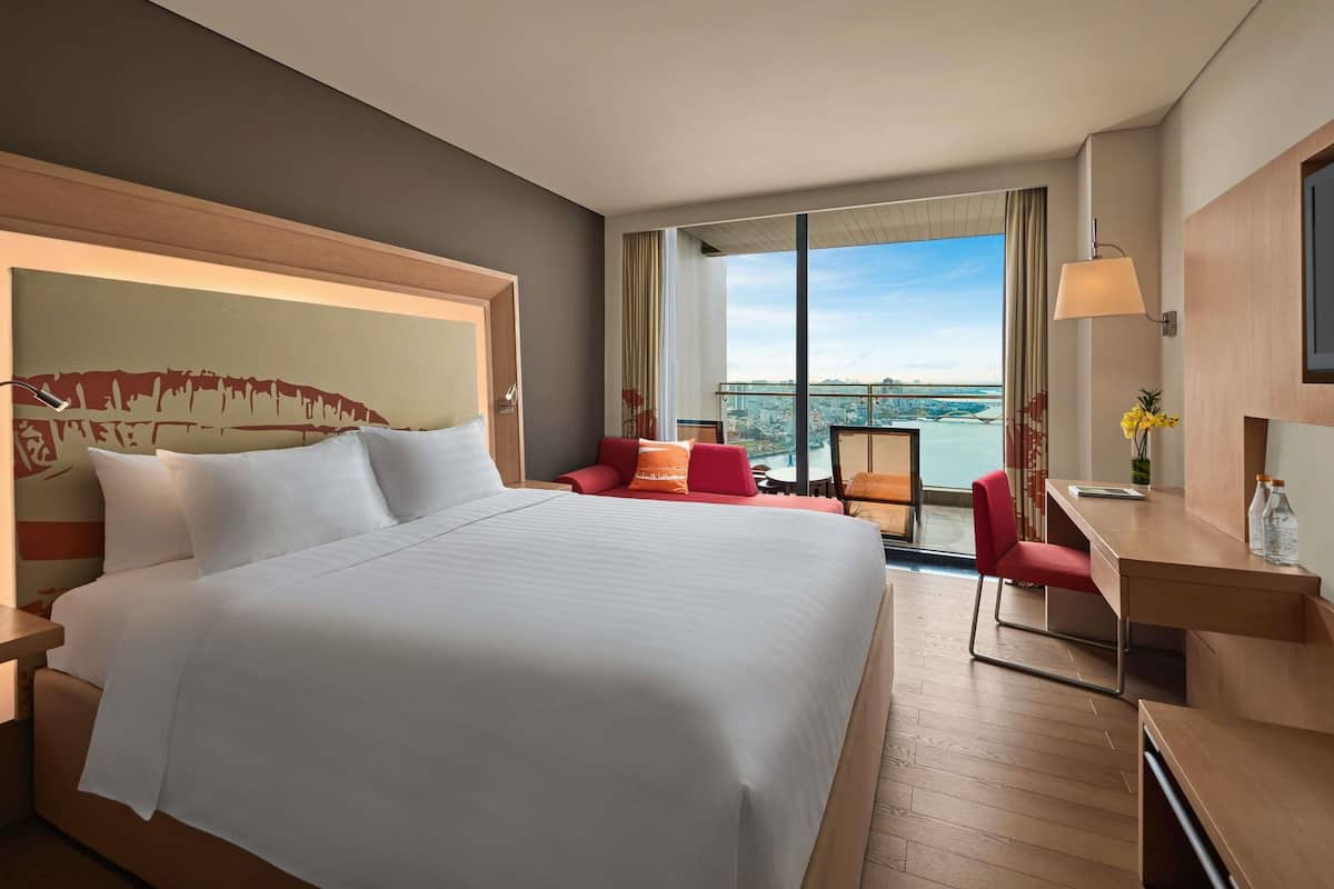Habitación de hotel con una cama grande, un escritorio, una silla y vistas a un paisaje urbano.
