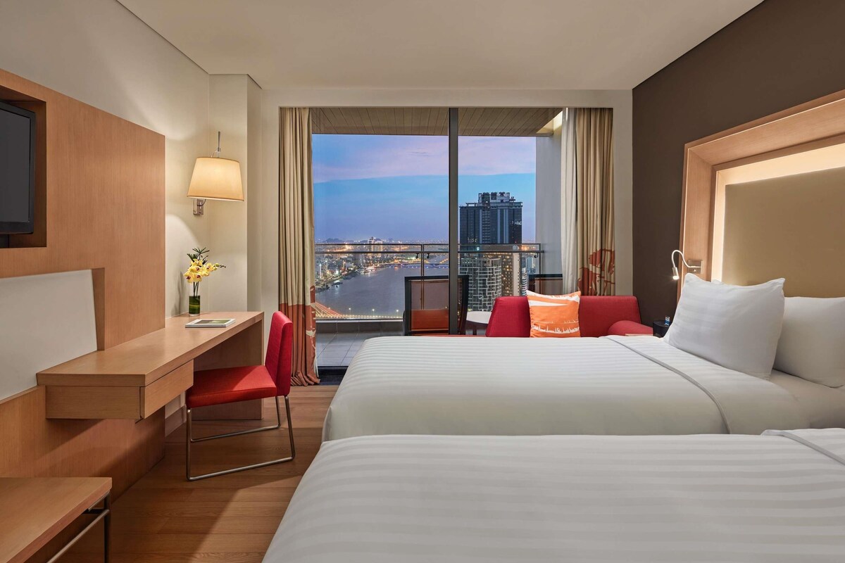 A hotel room with a large bed, a desk, a chair, and a TV.