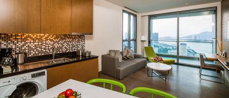 Una cocina moderna con lavadora, un comedor con mesa y sillas, y una sala de estar con sofá y vista a la ciudad.