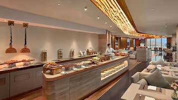 A modern hotel lobby with a central buffet, seating area, and a view of the sea.