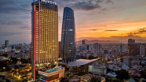 Um hotel moderno com um imponente letreiro 'NOVOTEL', uma piscina no terraço e um edifício de vidro próximo.