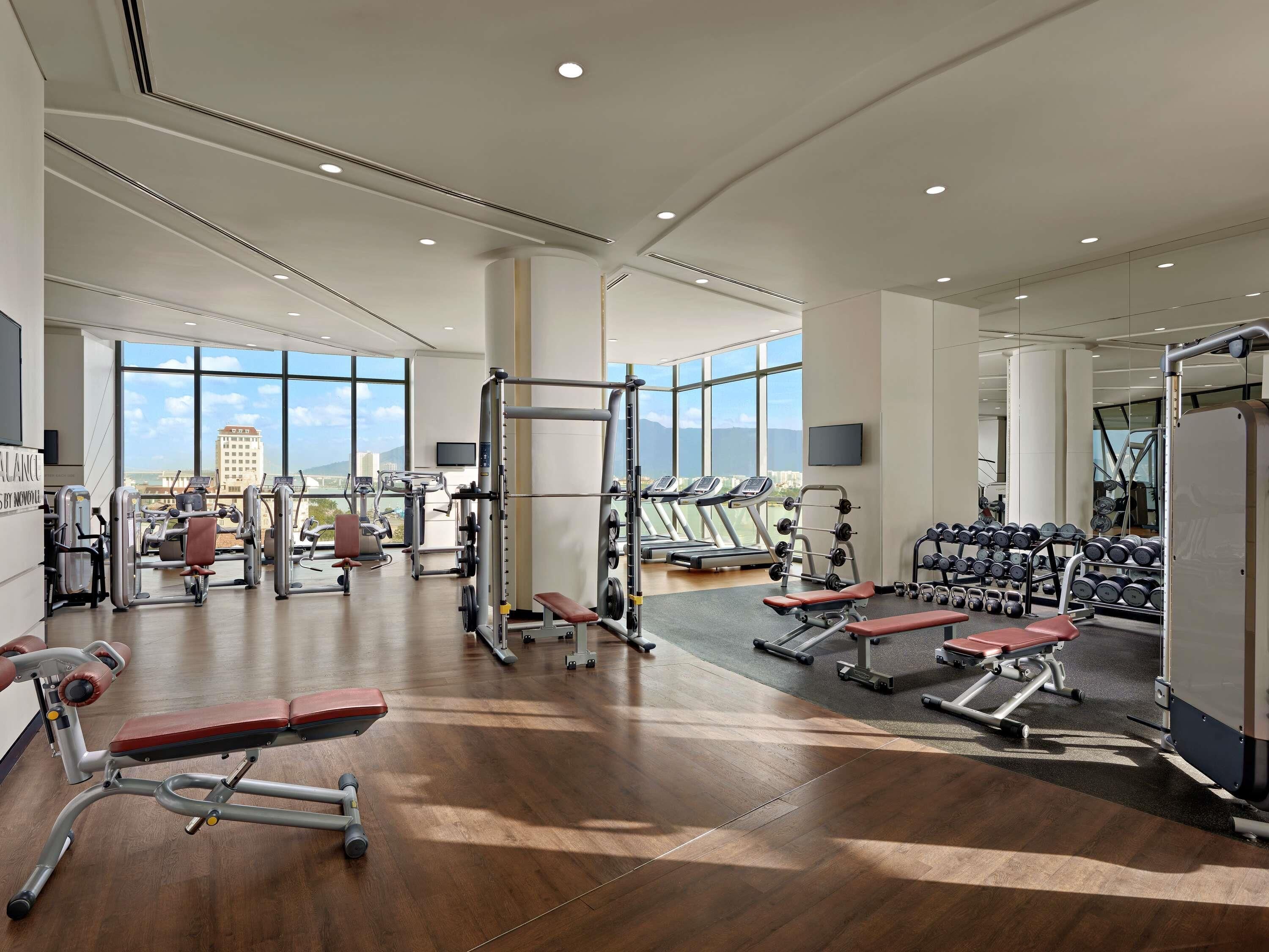 A spacious gym with cardio machines, weightlifting equipment, and a large window offering a city view.