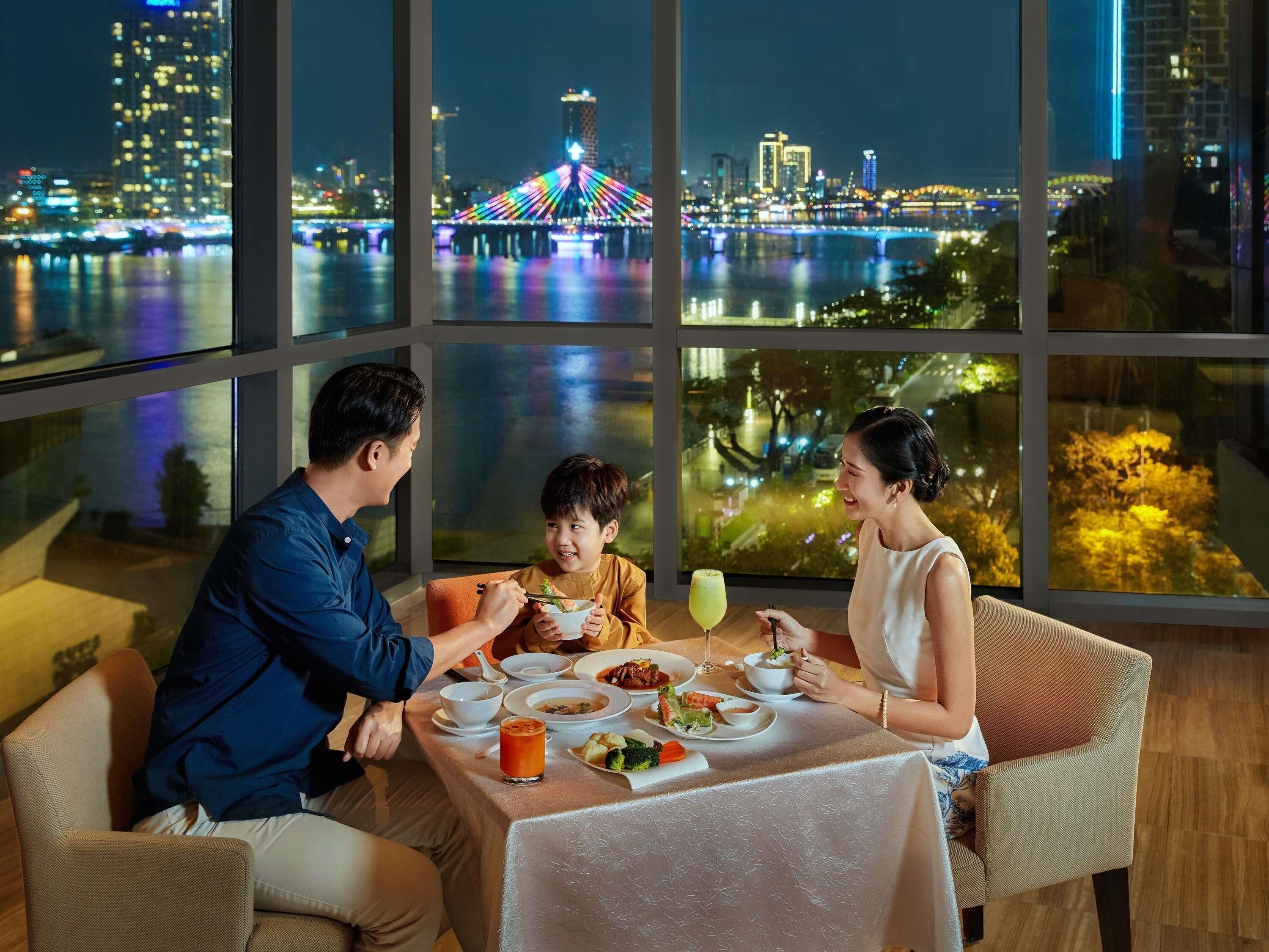 A dining room with a table set for three, large windows with a city view, and a table with various dishes and drinks.