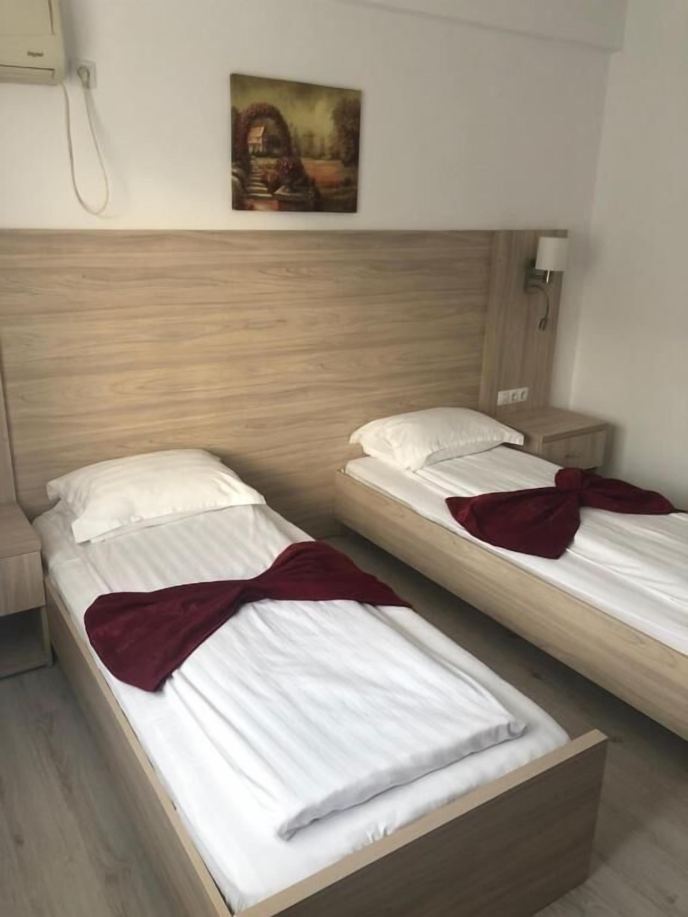 Two single beds with wooden headboards, white bedding, and a red throw blanket on each.