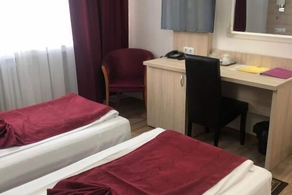A hotel room with two beds, a desk with a chair, a telephone, and a mirror.