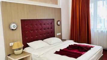 A hotel room with a large bed, a red headboard, a bedside lamp, and a window with curtains.