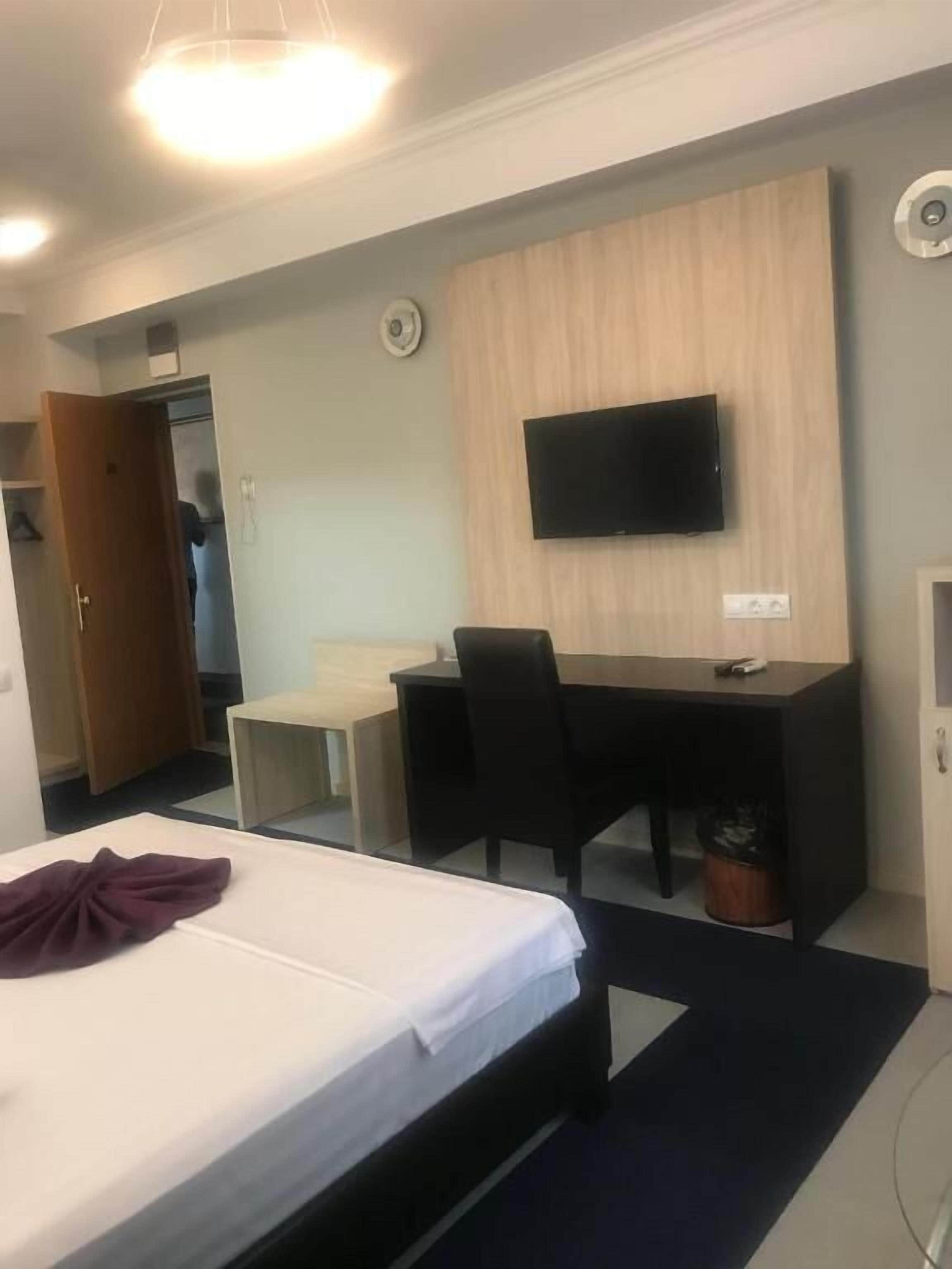A hotel room with a bed, a desk, a chair, a television, and a wardrobe.