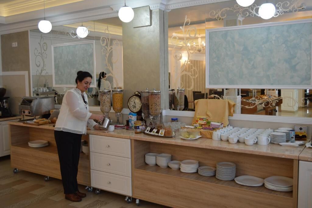 A buffet setup with a variety of food items and utensils, a person serving, and a mirror reflecting the room's decor.