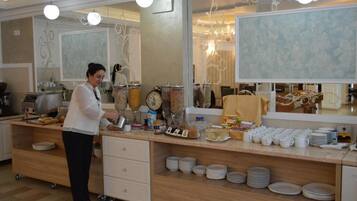 A buffet setup with a variety of food items and utensils, a person serving, and a mirror reflecting the room's decor.