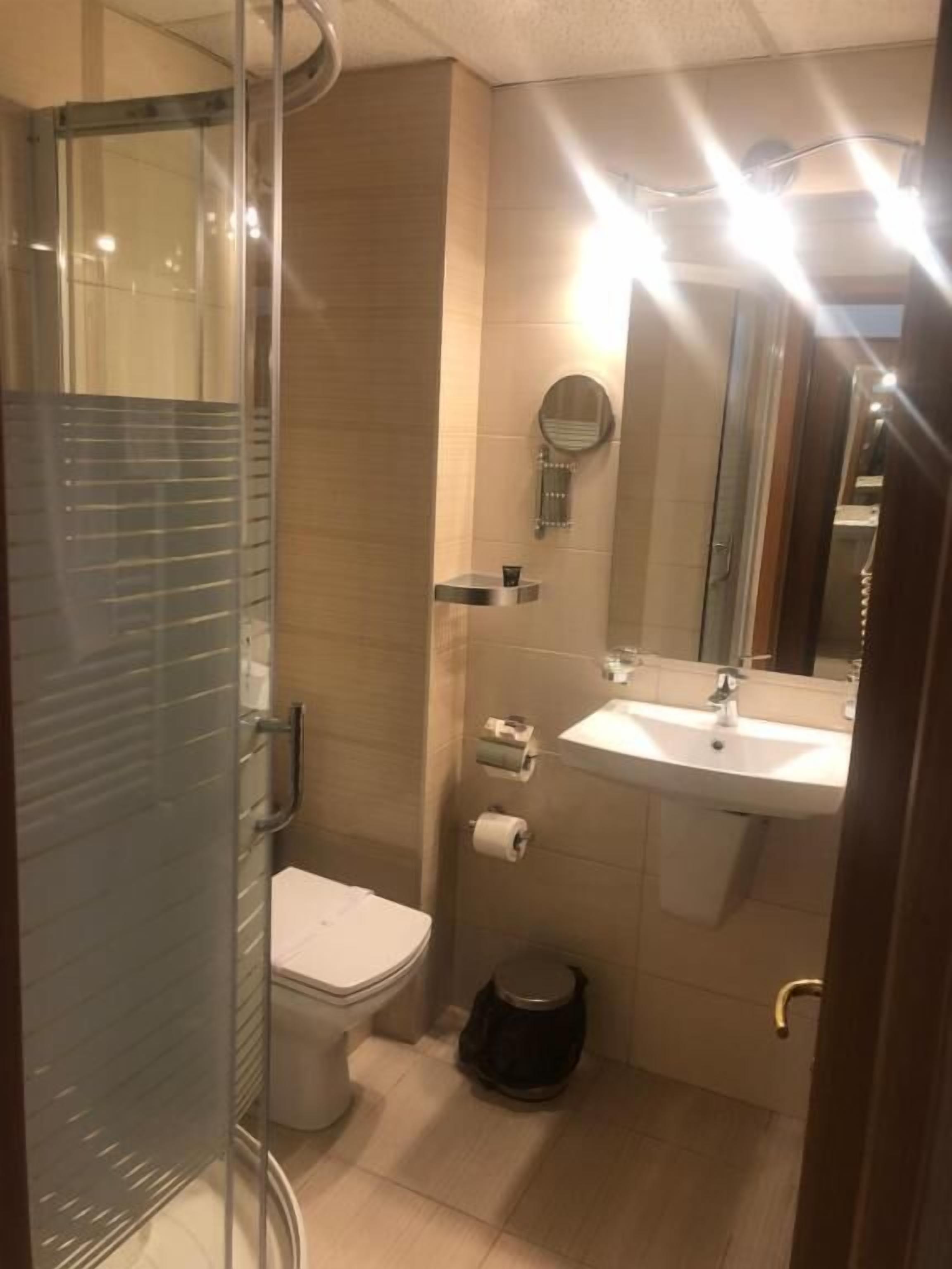 A compact bathroom with a glass shower enclosure, a toilet, a sink, and a mirror.