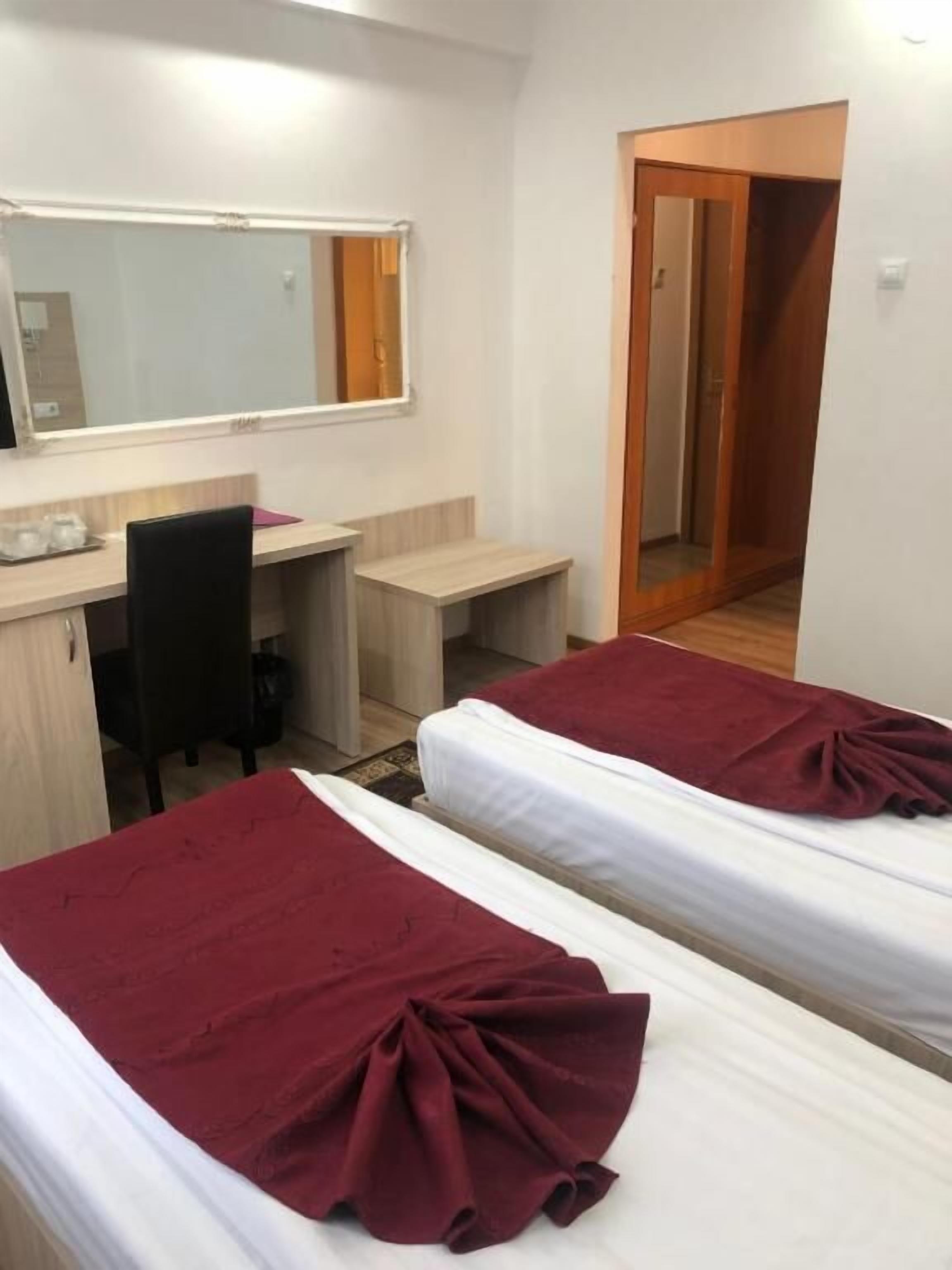 Habitación de hotel con dos camas individuales, un escritorio, una silla, un espejo y una puerta que da a otra habitación.