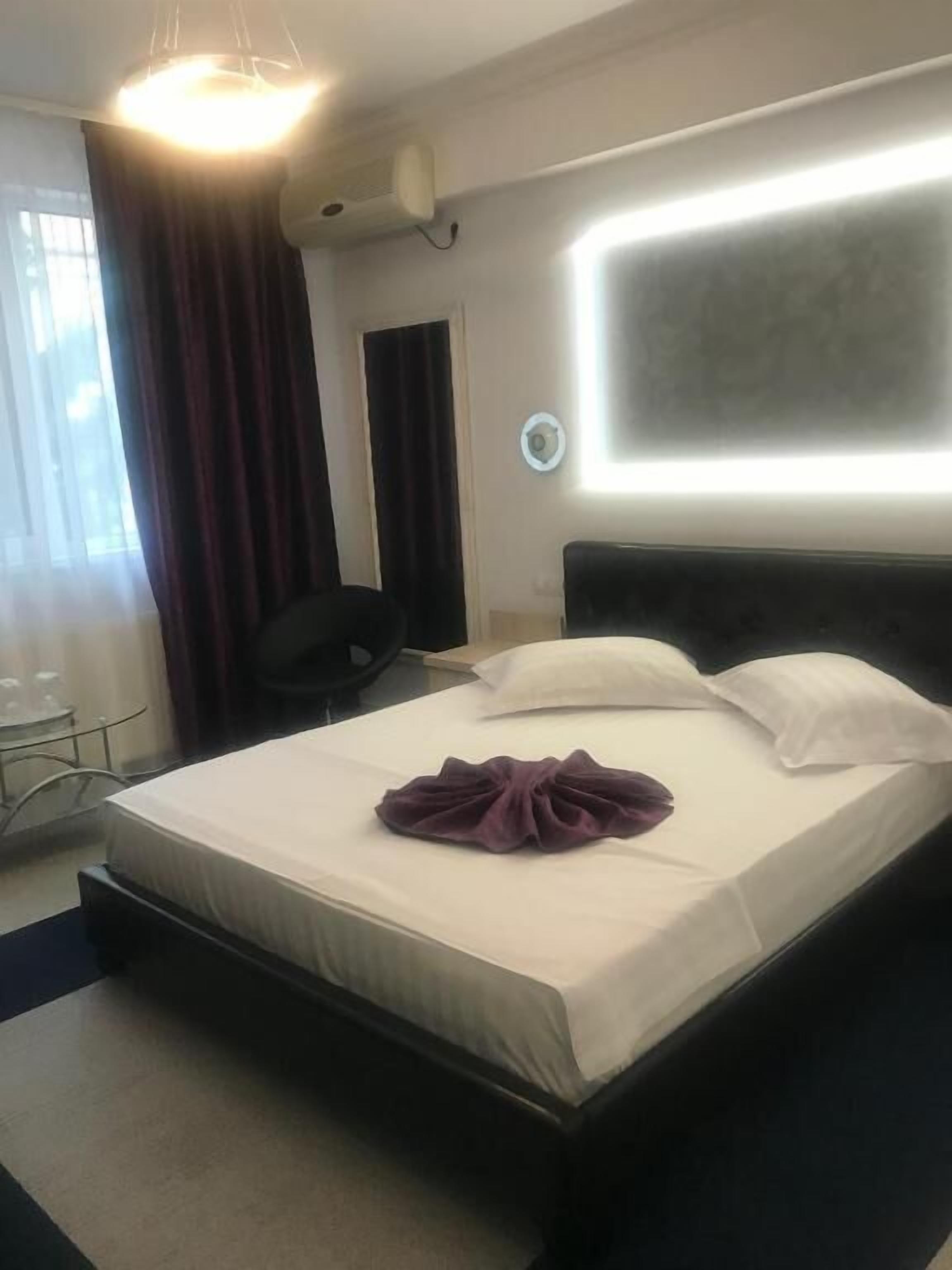 A hotel room with a bed, a desk, a chair, a window with curtains, and a wall-mounted air conditioner.