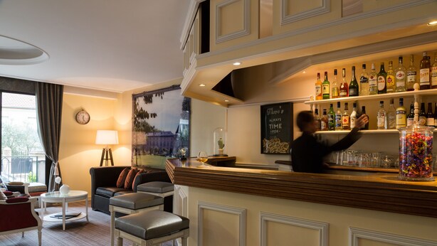 Un espace bar avec un barman, une étagère à bouteilles et un coin salon comprenant un canapé et des fauteuils.