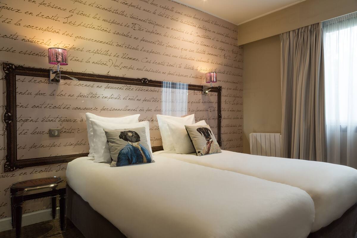 Een hotelkamer met twee bedden, een nachtkastje en een muur met decoratieve letters.