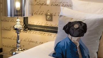 A bed with a white pillow featuring a blue embroidered design, a silver lamp, and a wall with cursive writing.