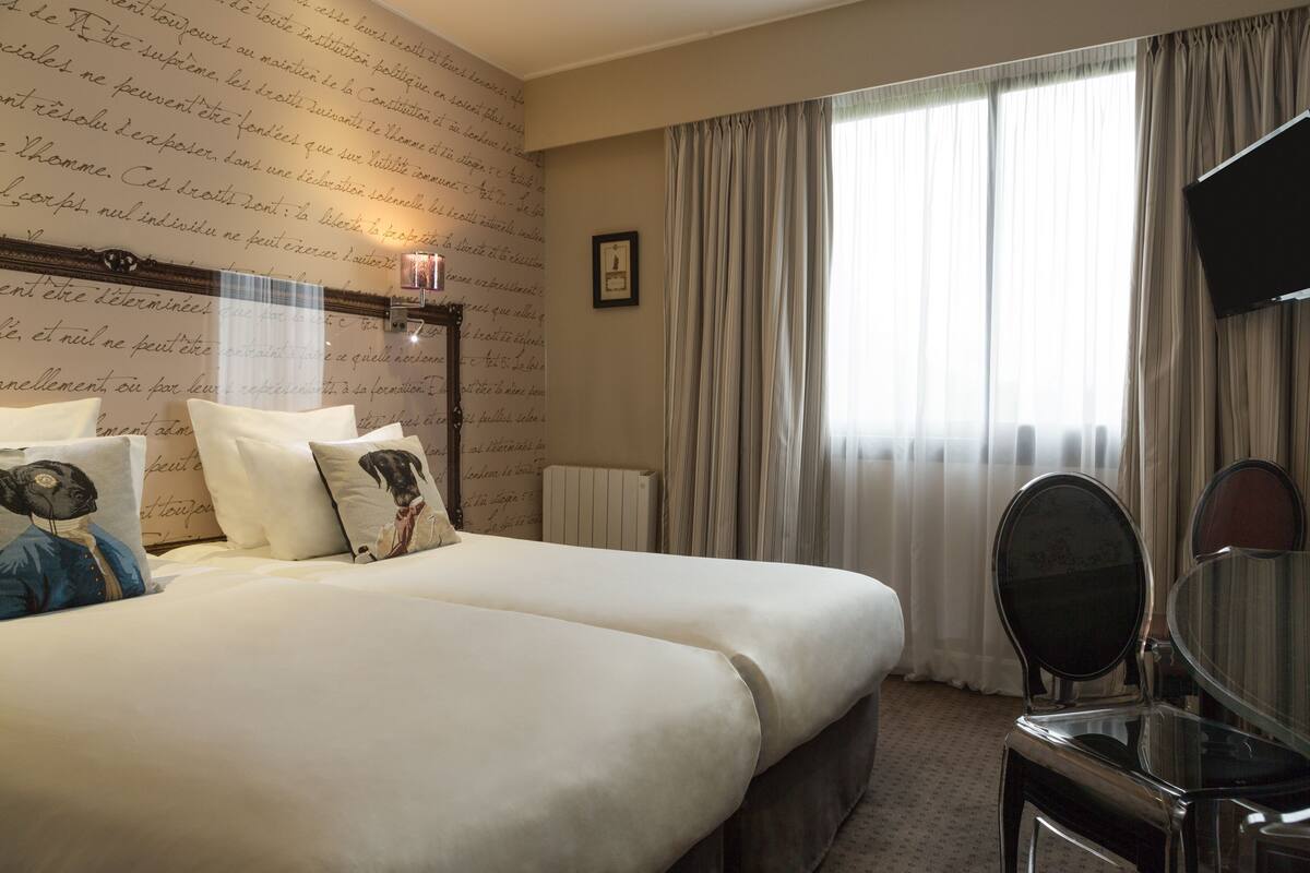 Een hotelkamer met een groot bed, een nachtkastje met spiegel en een raam met gordijnen.