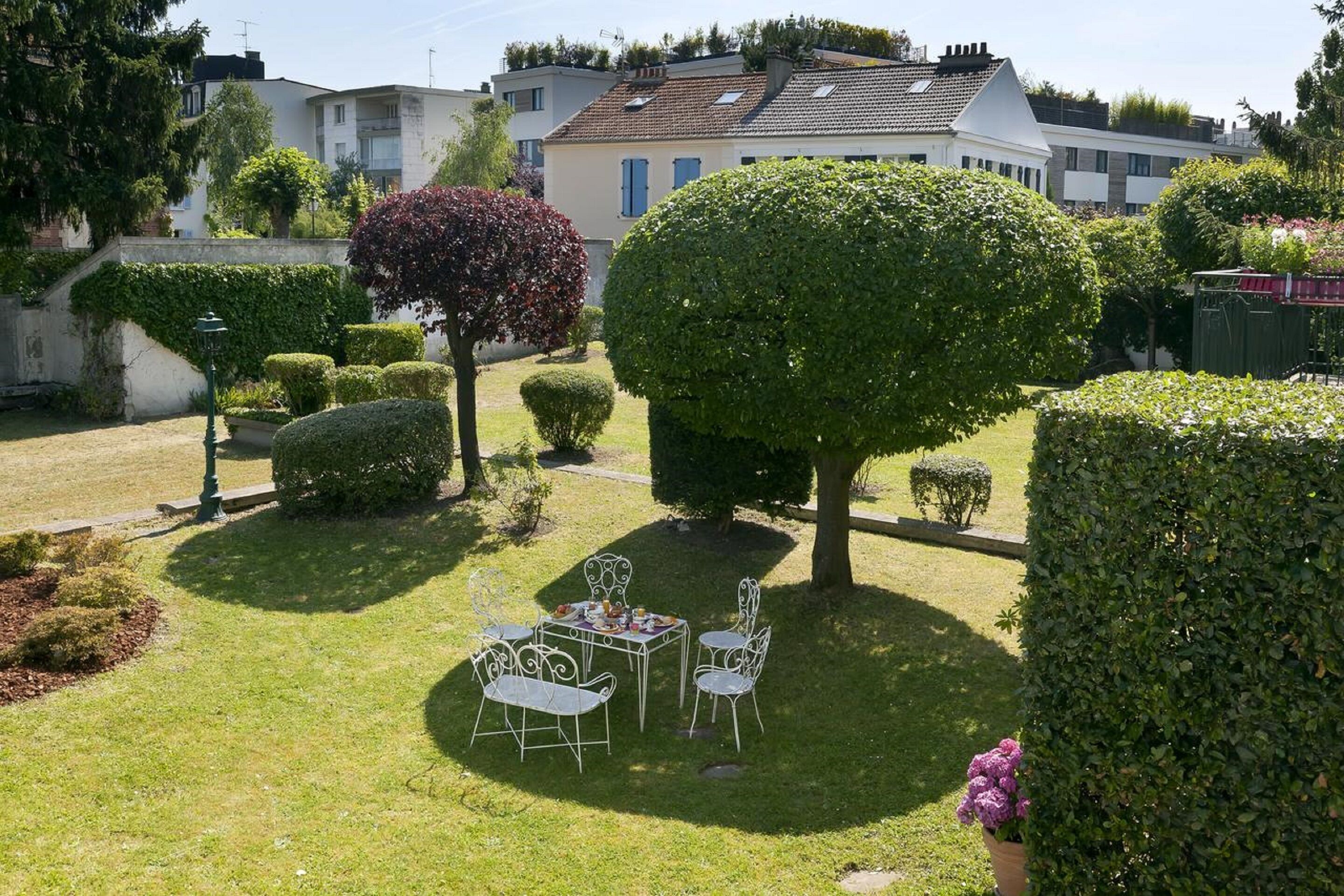 A well-maintained garden with a dining area featuring a table and chairs, surrounded by neatly trimmed hedges and trees.