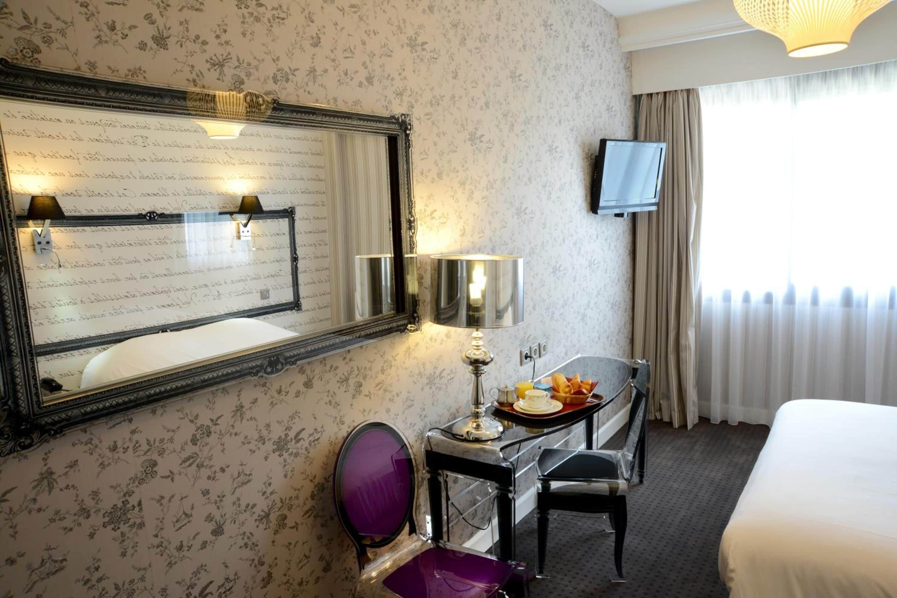 Une chambre d’hôtel avec un grand miroir, un bureau avec une lampe, une chaise, une télévision et un lit.