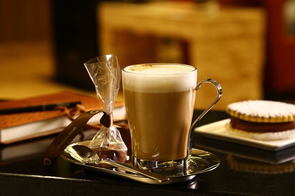 A cup of coffee on a saucer with a spoon beside it, a glass of water, and a dessert on a plate.